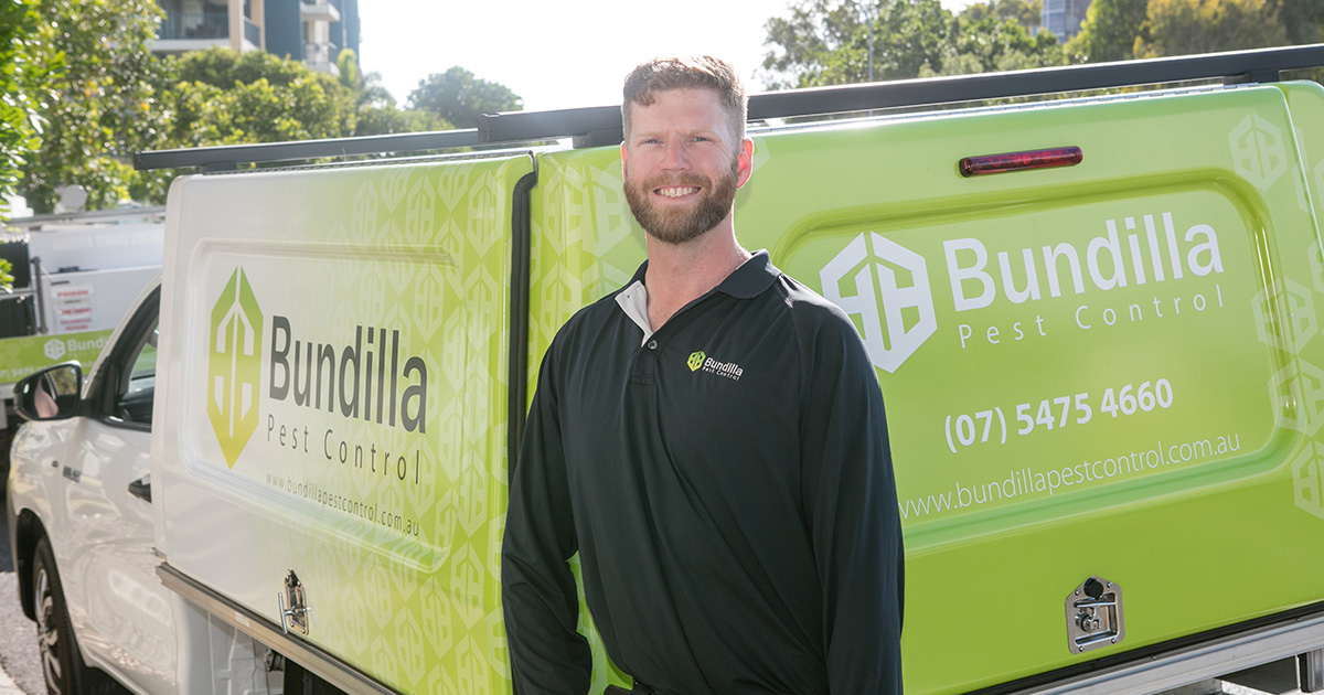 A Bundilla pest technician smiles while standing in front of a Bundilla vehicle